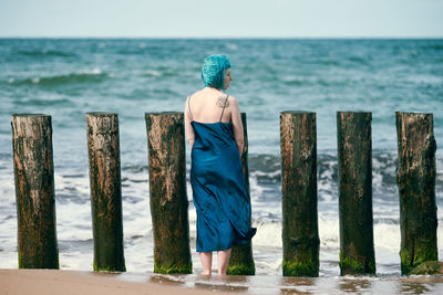 Young blue-haired woman in long dark blue dress with cute tattoo on her shoulder blade standing
