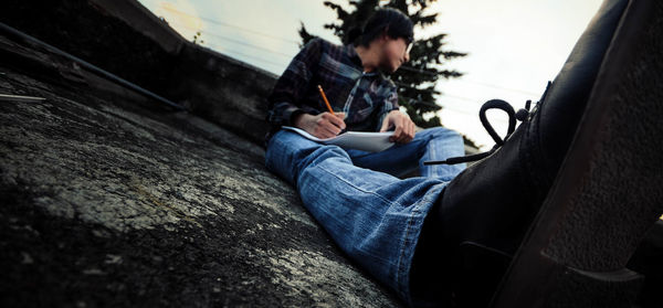 Surface level image of young man looking away while writing on paper at building terrace