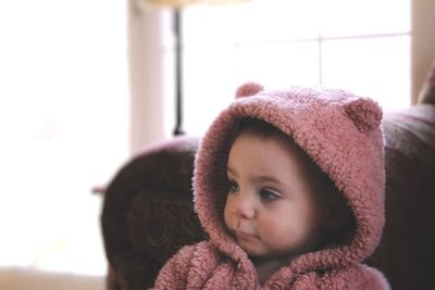 Cute girl looking away while sitting on seat at home