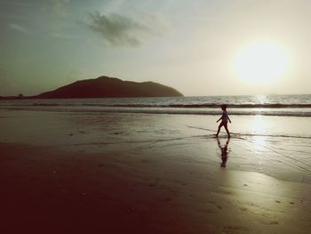 Side view of boy walking on shore at beach during sunset