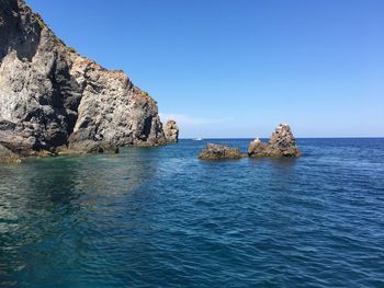 Rocks in sea against clear blue sky