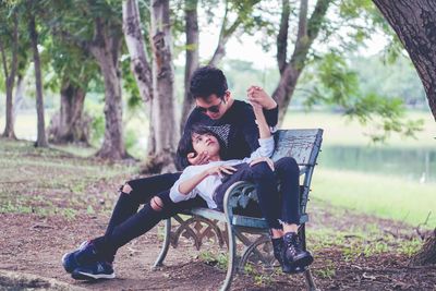 Full length of friends sitting on seat against trees