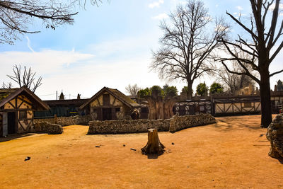 Bare trees and houses on field against sky