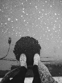 Low section of person standing by puddle on street during rainy season