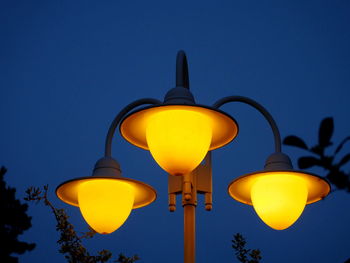 Low angle view of illuminated street light against clear blue sky