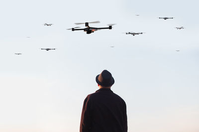 Rear view of man looking at drones flying in sky