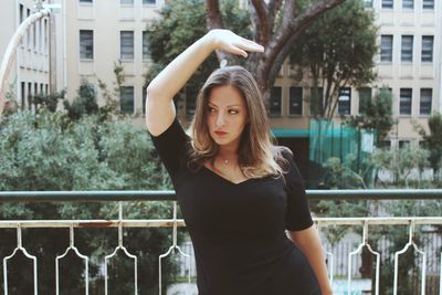 Portrait of young woman standing by railing in city