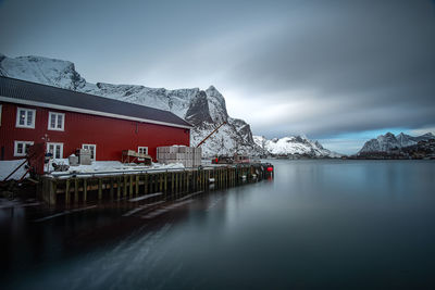 Built structure by lake against sky during winter