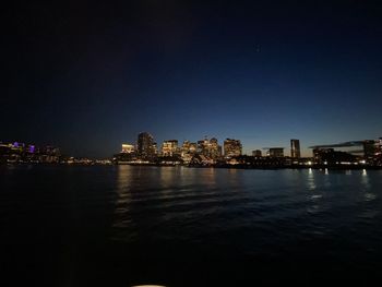 Illuminated buildings by sea against sky at night