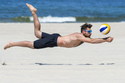 Shirtless man playing volleyball at beach