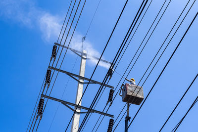 Low angle view of worker repairing electricity pylon cables from hydraulic platform