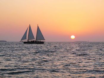 People sailing on sailboat in sea against clear sky during sunset