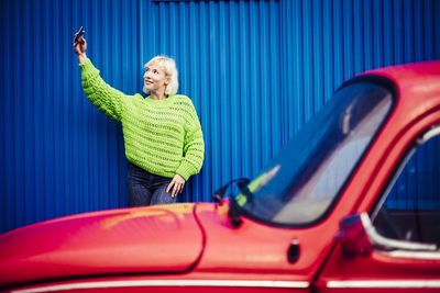 Woman taking selfie while standing by red car