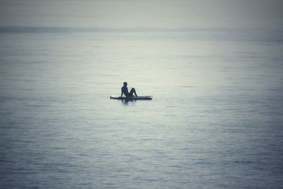 Silhouette of man sitting on sea against sky