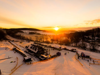 High angle view of houses on snow covered field against sky during sunset