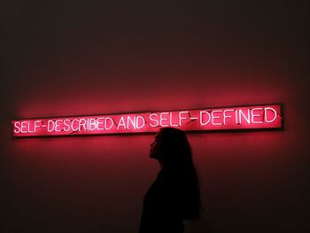 Rear view of woman standing against illuminated wall