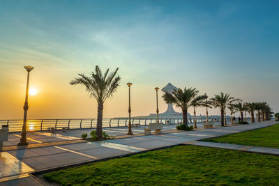 Palm trees by swimming pool against sky during sunset