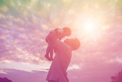 Low angle view of man holding pink umbrella against sky during sunset