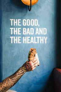 Crop unrecognizable person showing tasty sandwich to go against wall with the good the bad and the healthy inscription person