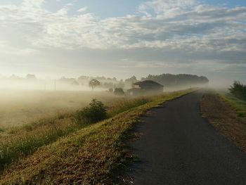 Empty road by field against cloudy sky during foggy weather