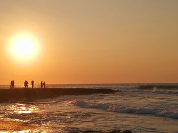 Silhouette people on beach against sky during sunset