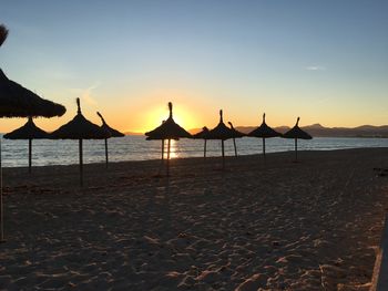 Silhouette parasols on beach against sky during sunset