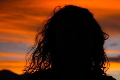 Close-up of silhouette woman with messy hair against orange sky during sunset