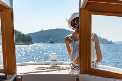 Rear view of young woman wearing summer clothes, sitting on bow of small boat