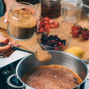 Woman cooking fruits and making homemade jam. putting brown sugar in the pot.