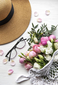 Straw hat and bouquet of pink rose flowers on white background. 