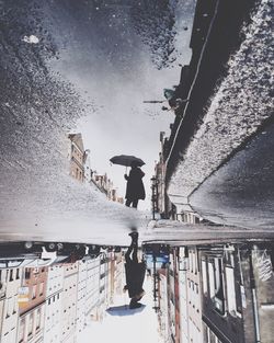 Reflection of woman with umbrella on puddle during rainy season
