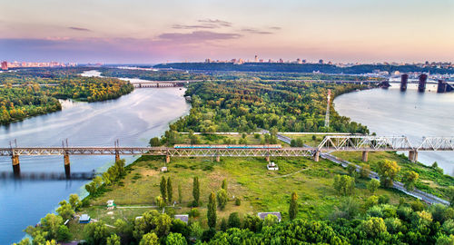 Bridge over river in city against sky at sunset