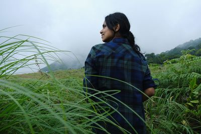 Side view of young woman standing on field against sky