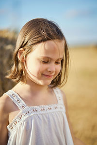 Cute little girl sits on mown rye in the field in summer