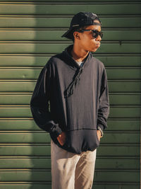 Young man wearing sunglasses standing against wall