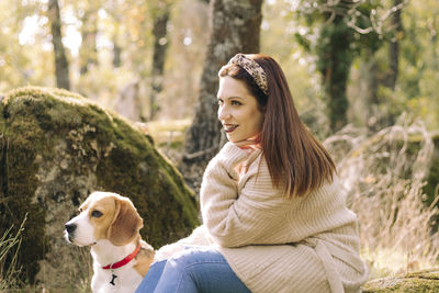 Smiling young woman, sitting next to her dog during a walk