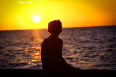 Silhouette boy on beach against sky during sunset