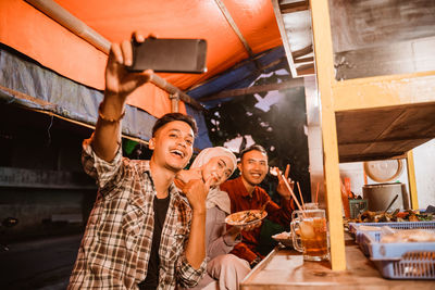 Smiling friends talking selfie while having food