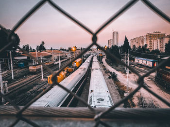 Train on railroad tracks against sky seen through chainlink fence