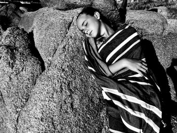 High angle view of girl wrapped in blanket lying on rock