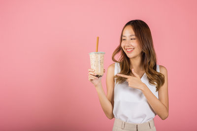Portrait of young woman drinking glass against pink background