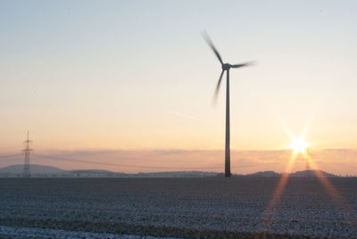 Wind turbines on field against sky during sunset