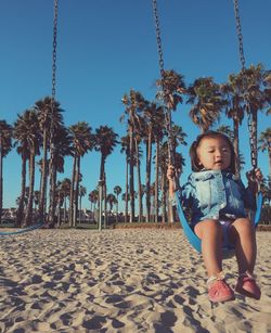 Girl on swing at beach against trees