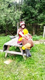 Smiling young woman sitting on grass against trees