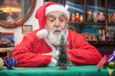 Senior man in santa claus costume sitting at home