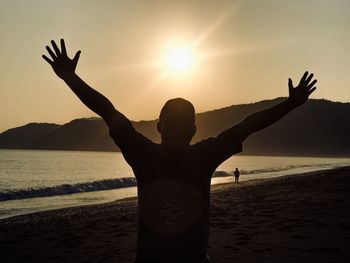 Man with arms outstretched standing at beach during sunset