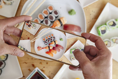 Blogger with mobile phone taking photo of delicious sushi on table, top view