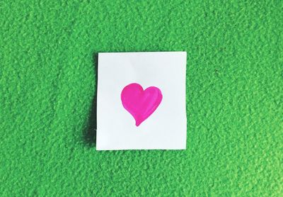 Close-up of white paper with heart shape on green wall