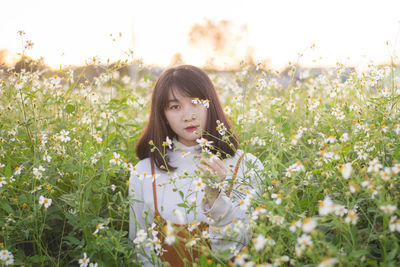 Portrait of young woman sitting in flowering field