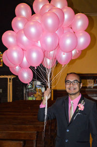 Portrait of smiling man with pink balloons at night